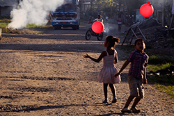 Niños juegan en la calle principal de Puerto Nuevo, Sucumbíos, mientras una pila de basura se quema al fondo. Foto: Misha Vallejo